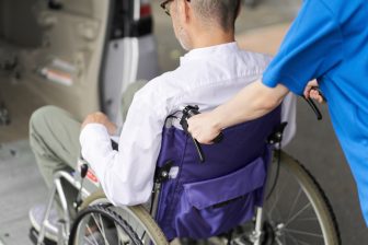 Beeld: Een persoon in een rolstoel wordt een busje inbegeleid