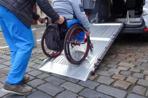 Een persoon in een rolstoel wordt een busje in begeleid